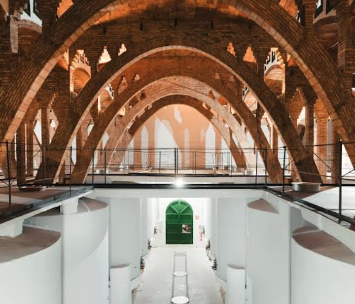 Interior of a brick vaulted hall with repeating arches and a white lower level, leading to a green door at the far end.