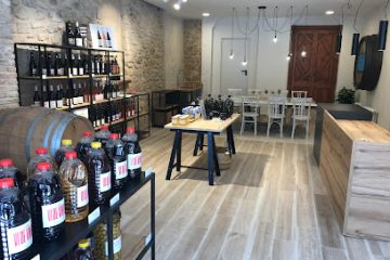Wine shop interior with bottle displays, a wooden barrel, and a tasting table in a rustic, airy space.