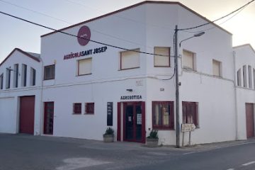 White corner storefront with red doors, signs 'Agrícola Sant Josep' and 'Agrobotiga' on a quiet street at dusk.
